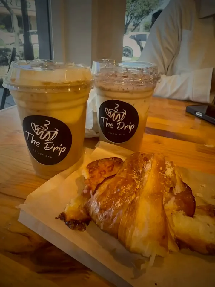 Two iced coffees and a croissant sandwich on a wooden table