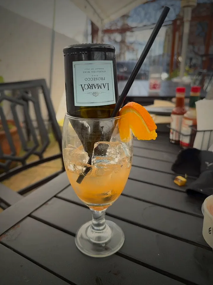 A spritz with an orange slice and a mini bottle upturned in the glass, on a patio