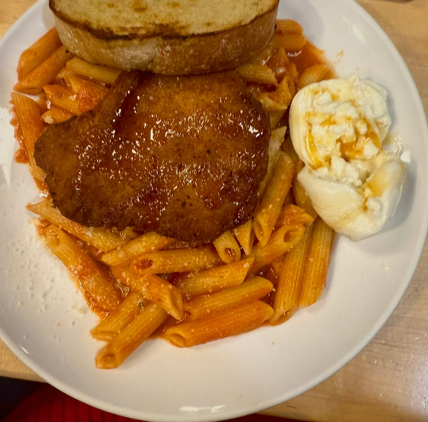 A breaded cutlet over penne in tomato sauce with burrata and grilled bread