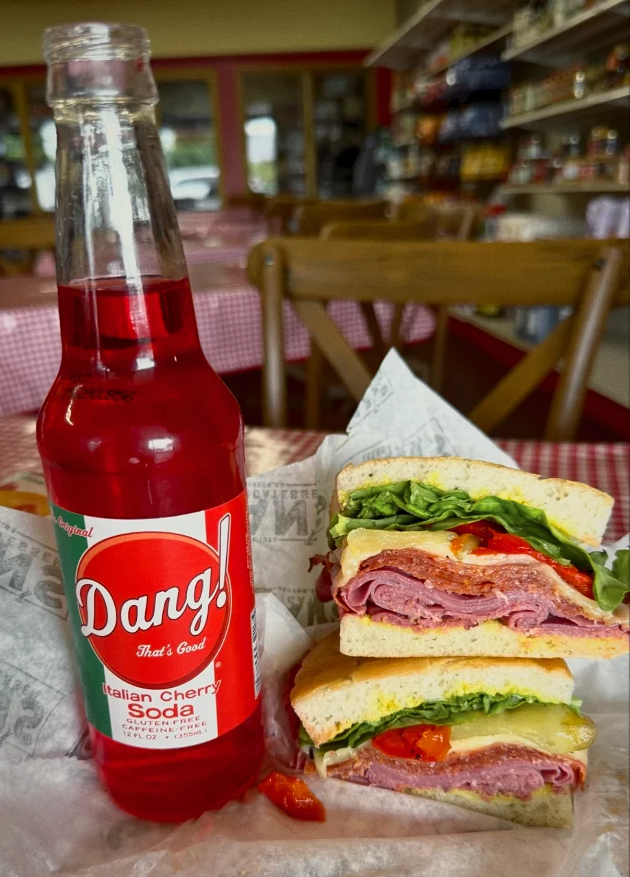 An Italian sub cut in half and stacked beside a bottle of cherry soda