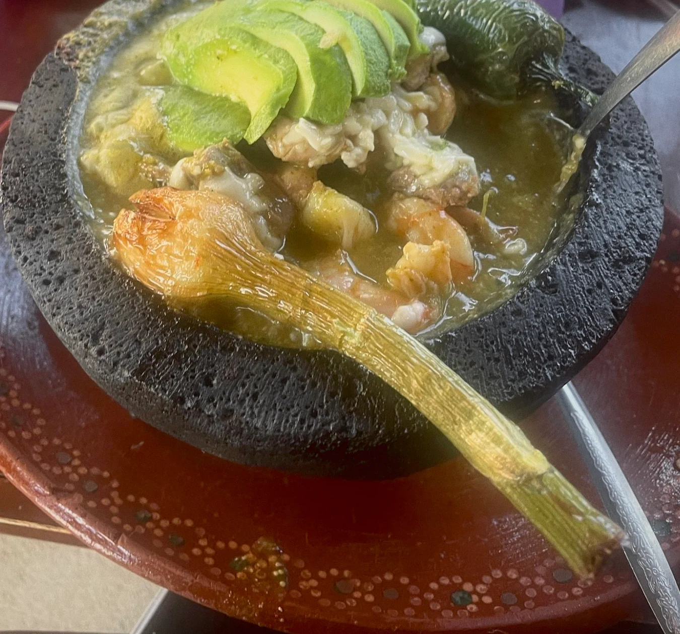 A molcajete with sliced avocado, shrimp, a roasted chile and grilled green onion